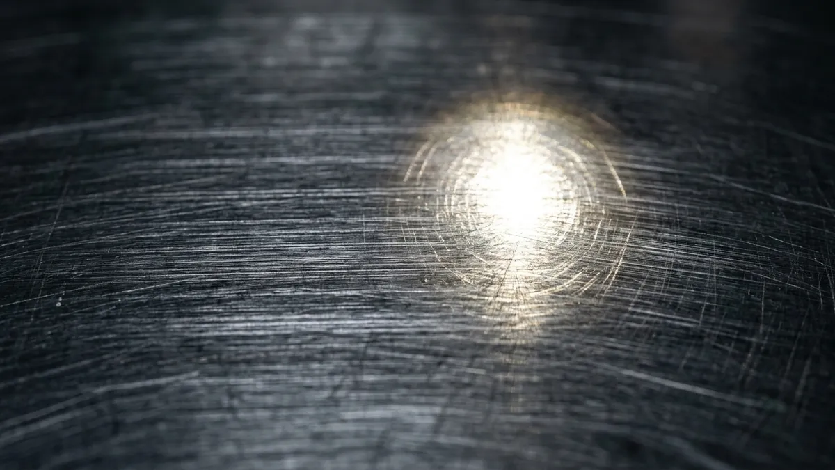 Detalhe em grande plano de uma chapa metálica de aço escovado com acabamento brilhante refletindo luz pontual.